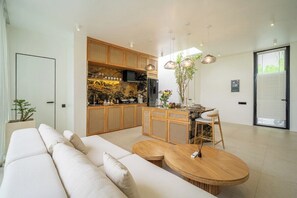 A modern kitchen with wooden cabinets, a dining area with a round table, and a living room with a sofa. - Modern 2BR in Ungasan's Best w Beach Access+Pool (Badung Regency)