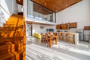 Eine moderne Küche mit Holzausstattung, ein Essbereich mit Holzstühlen und eine Treppe mit Holzstufen.