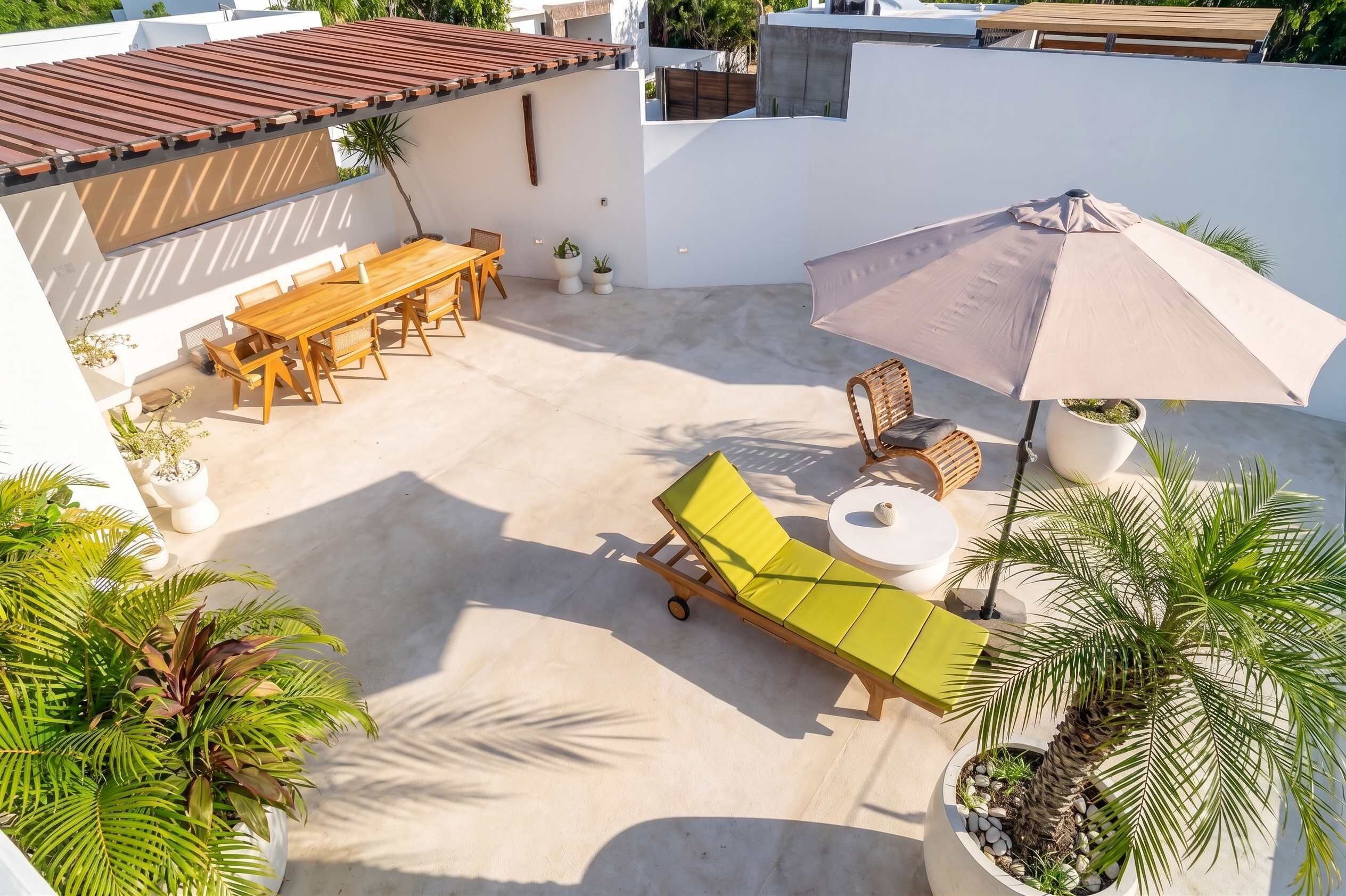 A rooftop patio with a wooden table and chairs, a lounge chair, and a large umbrella.