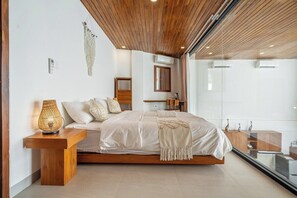 Ein modernes Schlafzimmer mit Holzboden, einem großen Bett mit Kopfteil, einem Nachttisch mit Lampe und Blick durch eine Glastür.