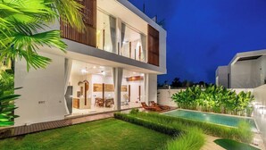 Una casa moderna de dos pisos con piscina, mobiliario exterior y un césped cuidado.