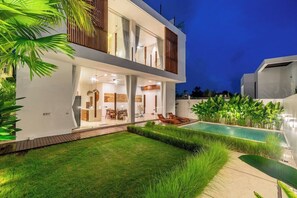 Ein modernes, zweistöckiges Haus mit Schwimmbad, Sitzgelegenheiten im Freien und einem gepflegten Rasen.