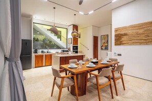 Een moderne keuken met een centraal eiland, een eethoek met een houten tafel en stoelen, en een trap die naar een hoger gelegen verdieping leidt.