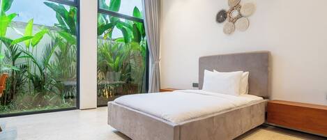 A modern bedroom with a large bed, a view of greenery through floor-to-ceiling windows, and a decorative wall piece.