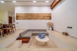 A modern living room with a sectional sofa, a round coffee table, and a large abstract wall art piece. - Modern 3BR villa - Ocean View & Rooftop, Pool (South Kuta)