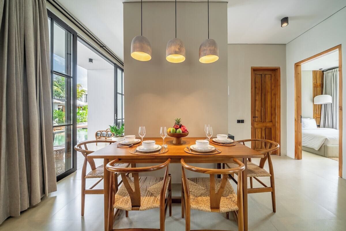 A dining area with a wooden table, six chairs, and hanging pendant lights.