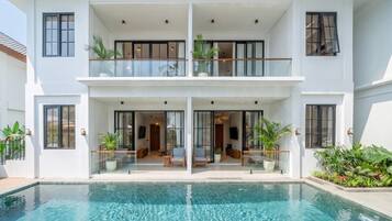 A two-story building with a swimming pool, balconies, and potted plants.
