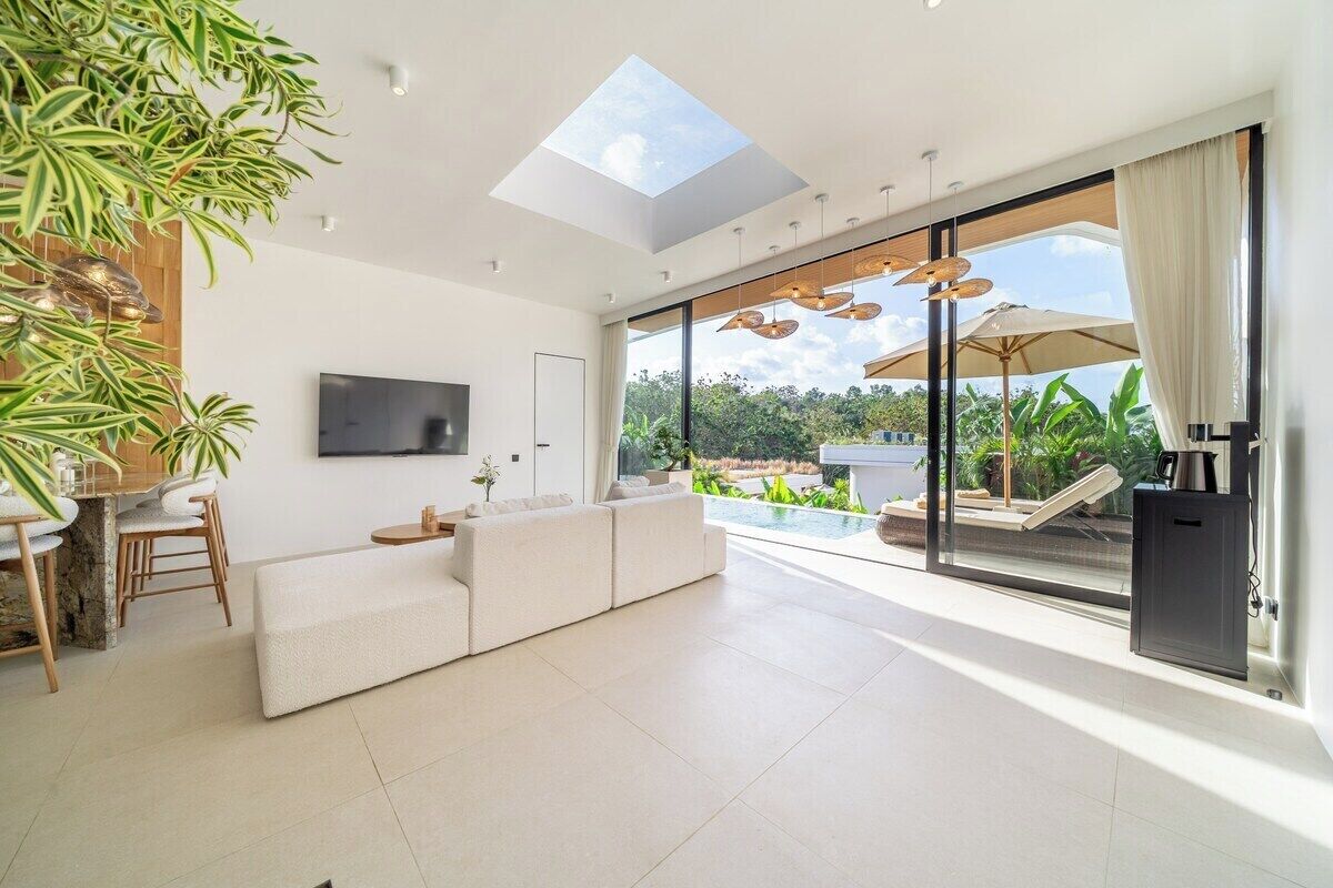 Una sala de estar moderna con televisor de pantalla plana, un sofá, un comedor con sillas y un amplio ventanal que da a una zona exterior con piscina.