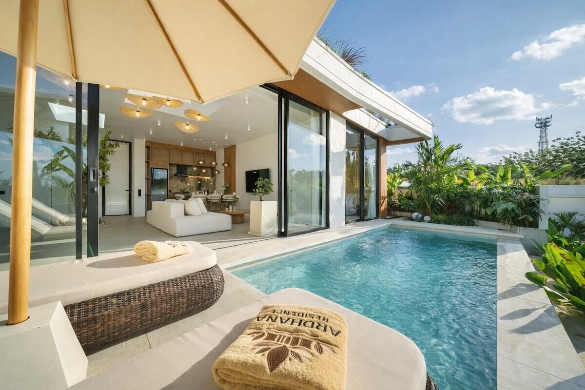 Zona moderna junto a la piscina con un espacio habitable con paredes de vidrio, piscina y una toalla con la marca 'ARAHANA'.