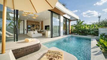 Zona moderna junto a la piscina con un espacio habitable con paredes de vidrio, piscina y una toalla con la marca 'ARAHANA'.
