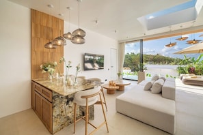A modern kitchen with a marble island, wooden panel wall, and a large window overlooking greenery. - Brand New Private 2BR Villa+Huge Pool+Beach Access (South Kuta)
