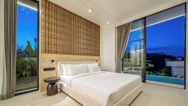 Una camera da letto moderna con un letto grande, una testata imbottita in legno, un piccolo tavolino e vista su una piscina.