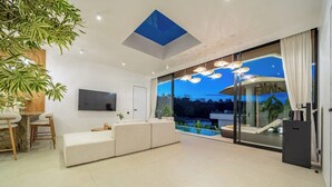 Un soggiorno moderno con un divano, un'area pranzo e un'ampia porta scorrevole in vetro che dà su una piscina.