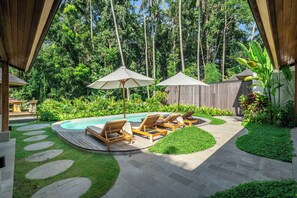 A pool area with lounge chairs and umbrellas, surrounded by lush greenery and a wooden fence. - New 3BR Villa Sorento+Top Ubud Location+Huge Pool (Gianyar Regency)