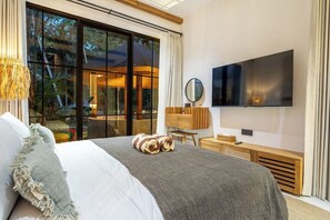 Ein modernes Schlafzimmer mit einem großen Bett, einem Flachbildfernseher und Blick ins Freie durch große Fenster.