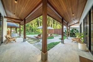 Ein überdachter Außenbereich mit Holzbalken, Liegestühlen, einem Pool und Topfpflanzen.