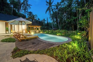 A swimming pool with lounge chairs and a covered seating area, surrounded by lush greenery and a wooden deck. - New 3BR Villa Sorento+Top Ubud Location+Huge Pool (Gianyar Regency)