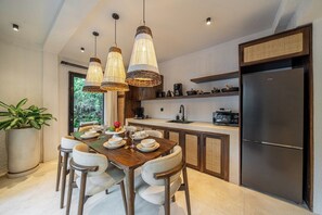 Eine moderne Küche mit Essbereich, ausgestattet mit einer großen Kochinsel, Pendelleuchten und einem eingebauten Kühlschrank.