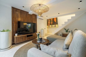 A modern living room with a flat-screen TV, a sofa, a coffee table, and a staircase. - Cozy 3BR Villa in Ubud w Garden Bath, Pool & Patio (Gianyar Regency)