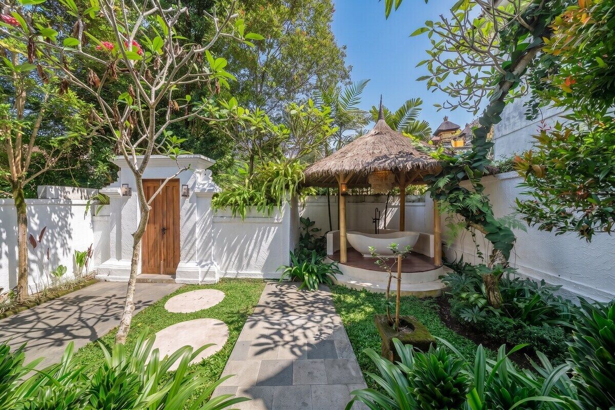 A garden with a thatched gazebo, a white wall, and a wooden door.