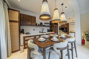 Cozinha moderna com área de refeições, apresentando uma mesa de madeira posta para quatro pessoas, luminárias pendentes de vime e um fogão embutido.