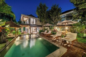 A pool area with lounge chairs and umbrellas, surrounded by lush greenery and a modern house. - Cozy 3BR Villa in Ubud w Garden Bath, Pool & Patio (Gianyar Regency)