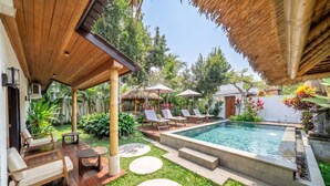Uma área de piscina com espreguiçadeiras, um espaço de estar coberto e um jardim bem cuidado.