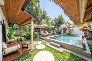 Ein Poolbereich mit Liegestühlen, einer überdachten Sitzgelegenheit und einem gepflegten Garten.