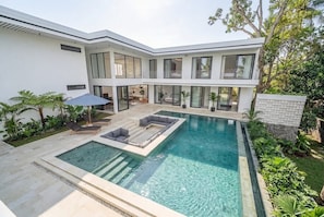 Ein modernes Haus mit Swimmingpool, Sitzgelegenheiten im Freien und üppiger Bepflanzung.