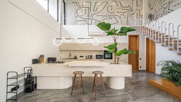 Eine moderne Küche mit einer zentralen Kochinsel, Barhocker und einer Treppe mit Geländer.