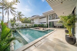 Ein moderner Poolbereich mit klarem Wasser, umgeben von Topfpflanzen und einer Terrasse.