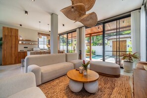 Ein modernes Wohnzimmer mit einer Couch, einem runden Couchtisch und einem Essbereich, im Hintergrund ist eine Küche zu sehen.