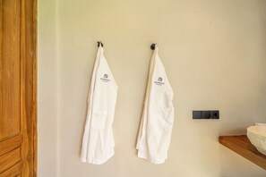 Deux serviettes blanches sont suspendues à des crochets sur un mur, une porte en bois et un évier en pierre sont posés sur un plan de travail en bois.