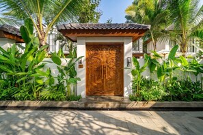 A traditional wooden gate with intricate carvings, flanked by lush tropical plants, leading to a building with a tiled roof. - Serene 2BR Villa in Ubud w Private Pool & Garden (Tegallalang)