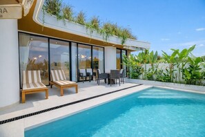 A modern pool area with lounge chairs and a dining table, surrounded by a white wall and greenery. - Minimalist 3BR Villa w Pool+Beach Access • Ungasan (Badung Regency)