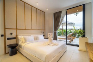 A modern hotel room with a large bed, a bedside table, a view of the outdoors, and a balcony with lounge chairs. - Minimalist 3BR Villa w Pool+Beach Access • Ungasan (Badung Regency)