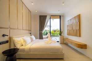 A modern hotel room with a large bed, a bedside table, a wall-mounted TV, and a view of the outdoors. - Minimalist 3BR Villa w Pool+Beach Access • Ungasan (Badung Regency)