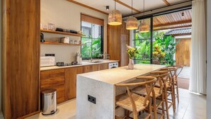 A modern kitchen with wooden cabinets, a marble countertop, and a dining area with wicker chairs. - Tropical 2BR Villa w Private Pool & Garden • Ubud (Gianyar Regency)