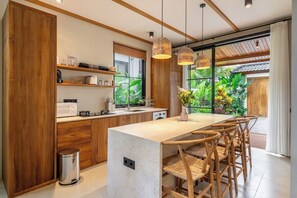 Eine moderne Küche mit Holzschränken, einer Marmorarbeitsplatte und einem Essbereich mit Korbstühlen.