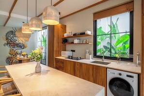 Eine moderne Küche mit Holzschränken, einer integrierten Waschmaschine und einem großen Fenster mit Blick auf Grünflächen.