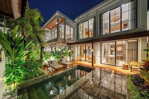 Ein modernes Haus mit Swimmingpool, großen Fenstern und einer Sitzgelegenheit im Freien.