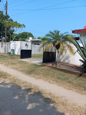 Un quartier résidentiel doté d’une entrée sécurisée, d’un palmier et d’un chemin piétonnier en béton.