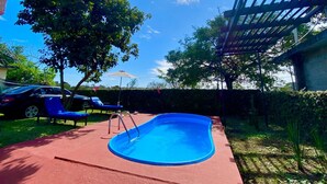 Ein Pool mit roter Liegefläche, umgeben von Bäumen und einer Pergola.