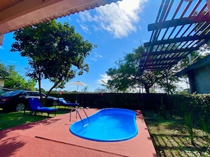 A swimming pool with a red deck, surrounded by trees and a pergola.