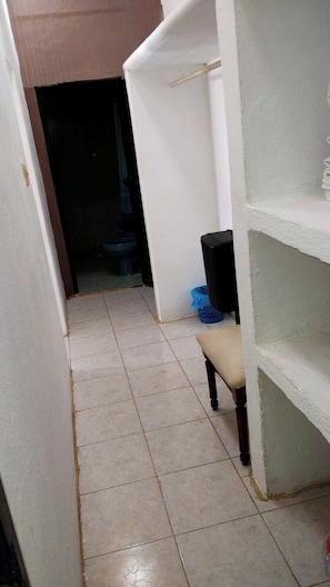 A narrow hallway with tiled flooring, a chair, and a black trash bin.