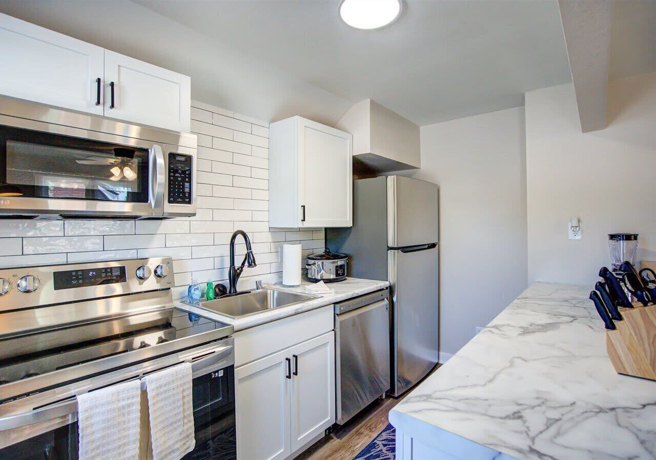 Contemporary kitchen with stainless steel appliances, subway tile backsplash, and sleek marble-look countertops. Fully stocked with cookware and utensils for easy meal preparation.
