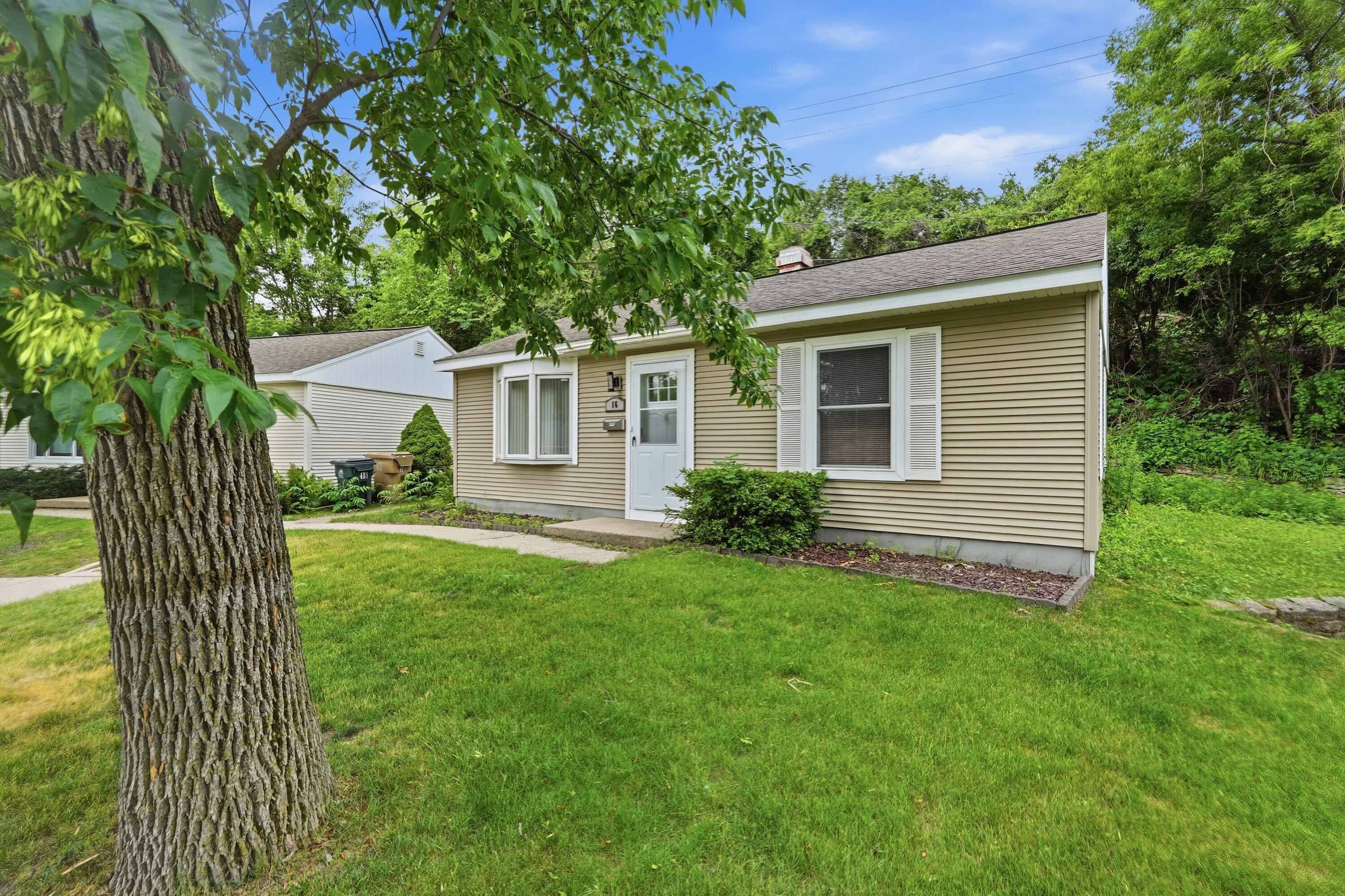 A single-story mobile home with a front porch, a small front yard, and a tree in the foreground.