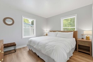 Ein Schlafzimmer mit einem großen Bett, zwei Nachttischen, einem Beistelltisch, einem runden Spiegel und einem Fenster mit Jalousien.