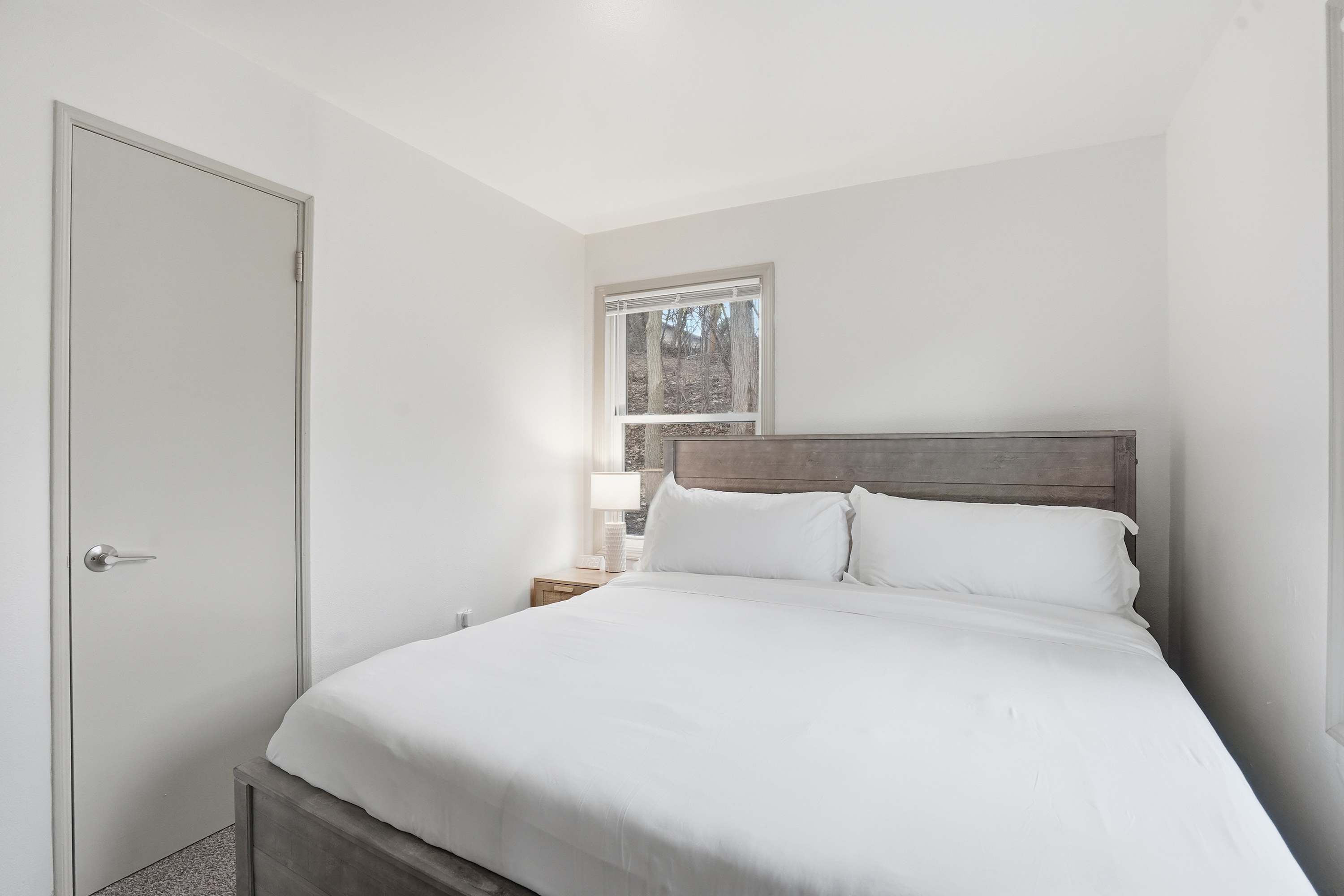 Une chambre à coucher avec un lit, une table de chevet, une lampe et une fenêtre.
