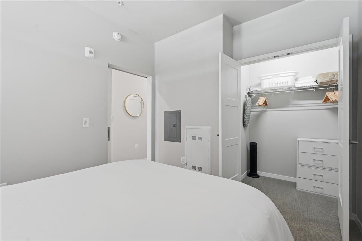 A bedroom with a bed, a closet with hanging space, and a door leading to another room.